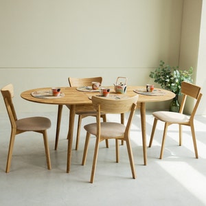 Peut inclure: Une table à manger ovale en bois clair avec quatre chaises. La table a une finition en bois naturel et les chaises ont un siège en tissu brun clair.
