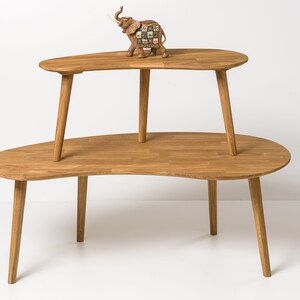 May include: A two-tiered wooden coffee table with a unique, organic shape. The table is made of natural wood and has a light brown finish. The top tier is slightly smaller than the bottom tier and is supported by four legs.