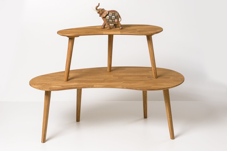 May include: A two-tiered wooden coffee table with a unique, organic shape. The table is made of natural wood and has a light brown finish. The top tier is slightly smaller than the bottom tier and is supported by four legs.
