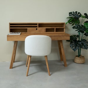 Peut inclure: Un bureau en bois clair avec une étagère intégrée et une chaise rembourrée blanche. Le bureau a un tiroir et plusieurs compartiments. Un livre intitulé "Green Brothers" est sur le bureau.