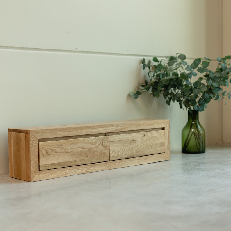 K&ouml;nnte beinhalten: Eine helle Holz-TV-Konsole mit zwei Schubladen. Die Konsole steht auf einem hellgrauen Betonboden.