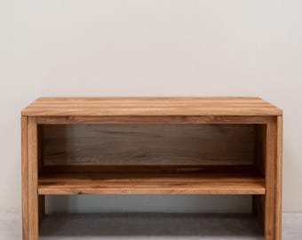 May include: A wooden shelf unit with a single shelf. The shelf is made of natural wood with a light brown finish. The shelf is freestanding and has a simple, modern design.