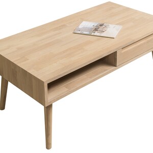 Puede incluir: Una mesa de centro de madera clara con un caj&oacute;n y un estante. La mesa tiene cuatro patas y una tapa rectangular.