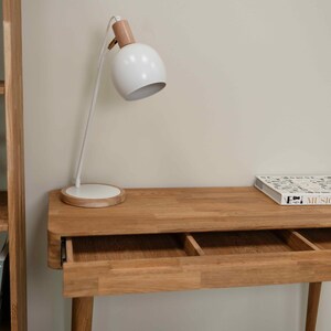 May include: A light wood desk with two drawers, a white lamp with a wooden base, and a book titled "Music" on the surface.