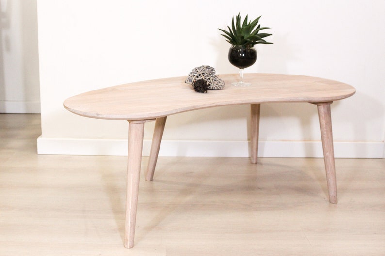 May include: A light wood coffee table with a unique, organic shape and four tapered legs. The table is made of natural wood and has a light, airy feel.