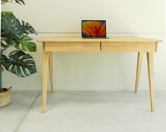 May include: A light wood desk with two drawers and tapered legs. A laptop computer is on the desk.