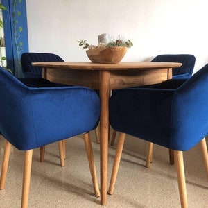 May include: A round wooden dining table with four blue velvet chairs. The chairs have wooden legs and a curved back.