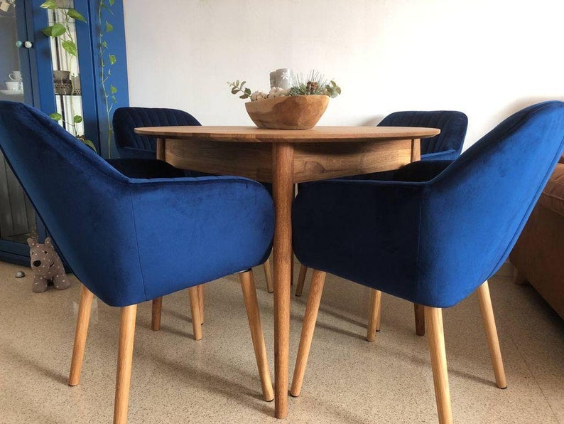 May include: A round wooden dining table with four blue velvet chairs. The chairs have wooden legs and a curved back.