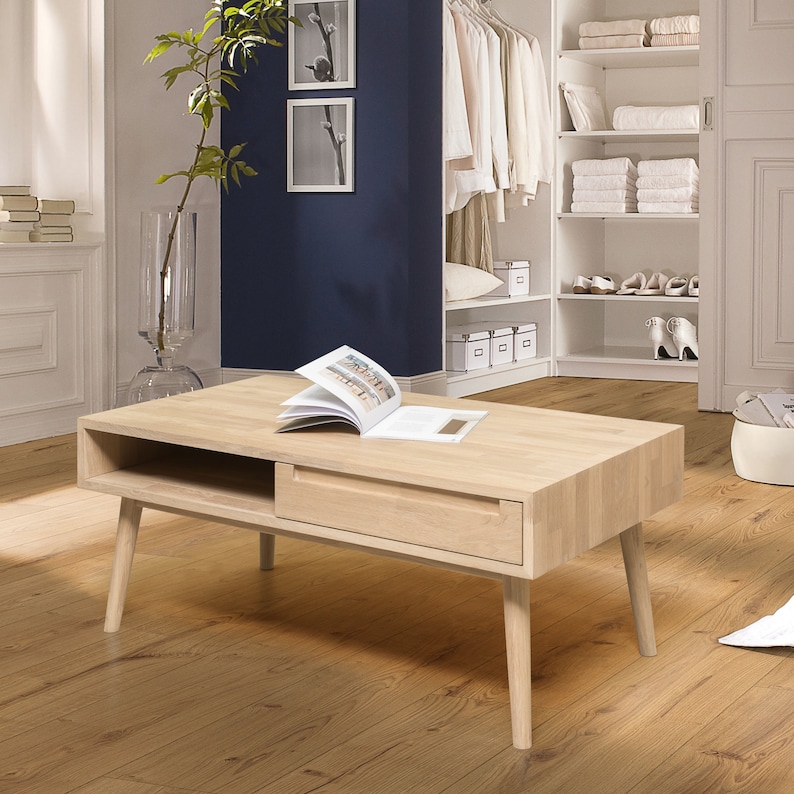 Puede incluir: Una mesa de centro de madera clara con un caj&oacute;n y un estante. La mesa tiene un dise&ntilde;o moderno con patas c&oacute;nicas.