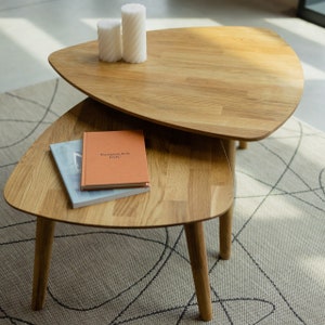 Puede incluir: Dos mesas triangulares de madera anidadas con un libro en la mesa inferior y dos velas blancas en la mesa superior.