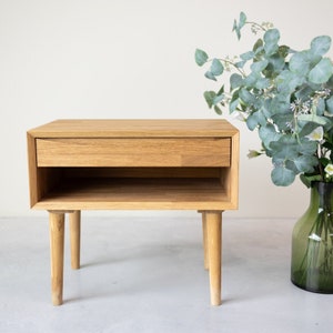 May include: A light wood nightstand with a single drawer and a lower shelf. The nightstand has four legs and is made of solid wood.