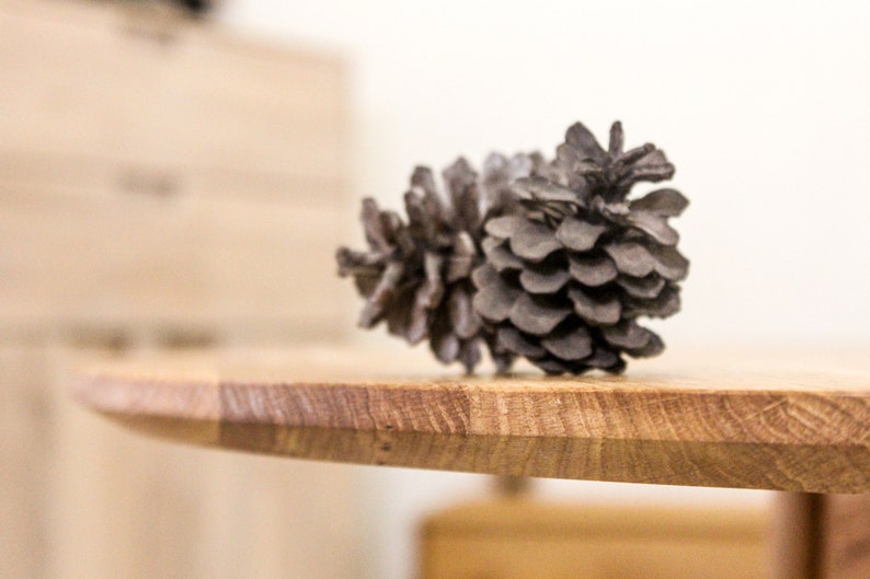 May include: A gray pine cone sits on a wooden table top. The table is made of light brown wood with a natural grain pattern.
