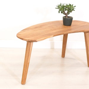 May include: A wooden coffee table with a unique, asymmetrical, kidney-shaped top and three legs. The table is made of light brown wood and has a natural finish.