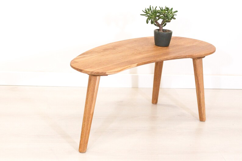 May include: A wooden coffee table with a unique, asymmetrical, kidney-shaped top and three legs. The table is made of light brown wood and has a natural finish.