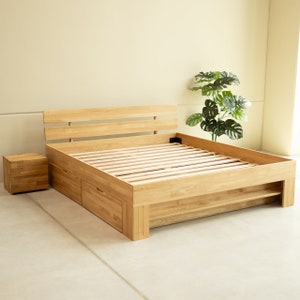 May include: A wooden bed frame with a slatted headboard and a storage drawer underneath. The bed frame is made of natural wood and has a light brown finish.