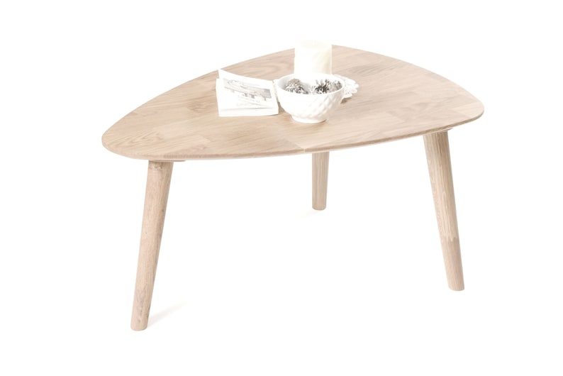 Puede incluir: Una mesa de centro triangular de madera clara con tres patas. La mesa tiene un taz&oacute;n blanco con art&iacute;culos decorativos en la parte superior.
