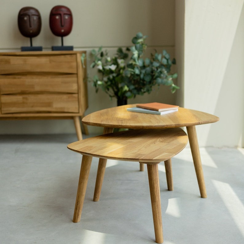 Puede incluir: Dos mesas de centro de madera con tapas triangulares. Las mesas son de madera marr&oacute;n claro y tienen un acabado natural. La mesa superior tiene dos libros encima.