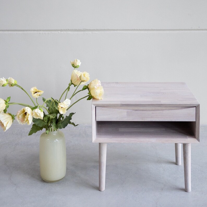 May include: A white wooden nightstand with a drawer and a shelf. The nightstand has a simple design and is perfect for a bedroom.