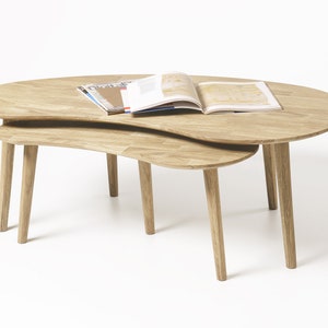 May include: Two wooden nesting coffee tables with a unique, organic shape. The top table has a magazine and a book on it.