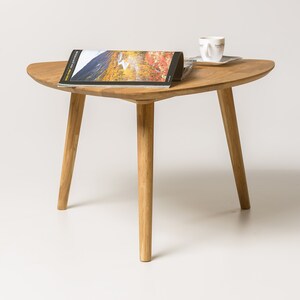 Puede incluir: Una mesa de centro de madera con una tapa triangular y tres patas. La mesa est&aacute; hecha de madera marr&oacute;n claro y tiene un acabado natural. Una revista y una taza y un platillo est&aacute;n sobre la mesa.