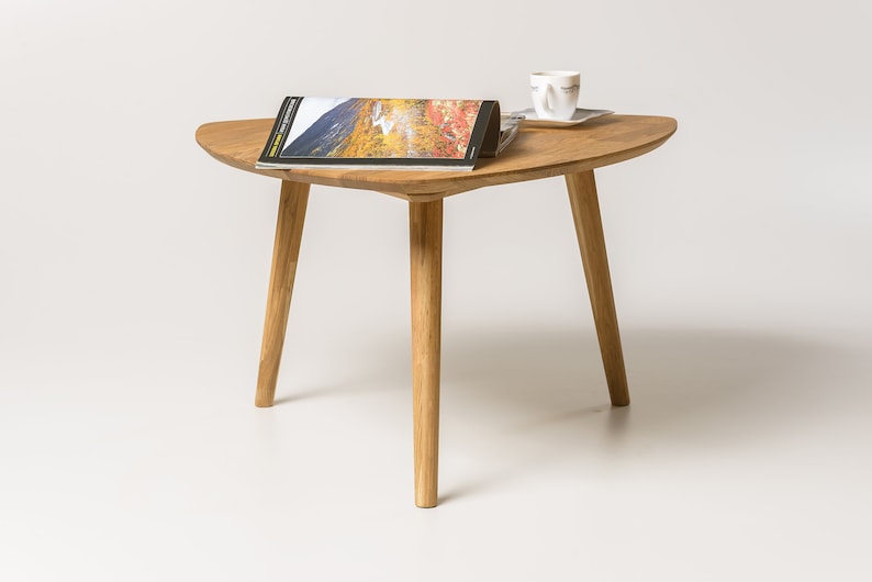 Puede incluir: Una mesa de centro de madera con una tapa triangular y tres patas. La mesa est&aacute; hecha de madera marr&oacute;n claro y tiene un acabado natural. Una revista y una taza y un platillo est&aacute;n sobre la mesa.