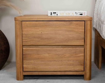 May include: A light brown wooden nightstand with two drawers. The nightstand has a book titled "Musica" on top.