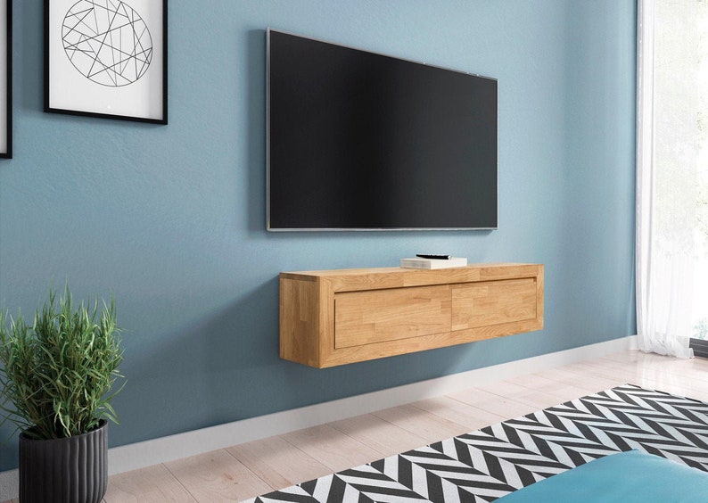 K&ouml;nnte beinhalten: Ein schwebendes Regal aus hellem Holz mit zwei Schubladen, montiert an einer blauen Wand unter einem Flachbildfernseher.