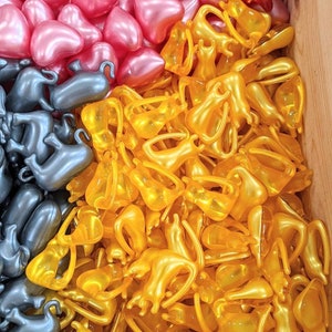 K&ouml;nnte beinhalten: Nahaufnahme eines Stapels kleiner, goldener, herzf&ouml;rmiger Kapseln. Die Kapseln sind in einem zuf&auml;lligen Muster angeordnet und alle gleich gro&szlig; und gleich geformt. Die Kapseln bestehen aus einem klaren, gl&auml;nzenden Material und haben einen leichten Schimmer.