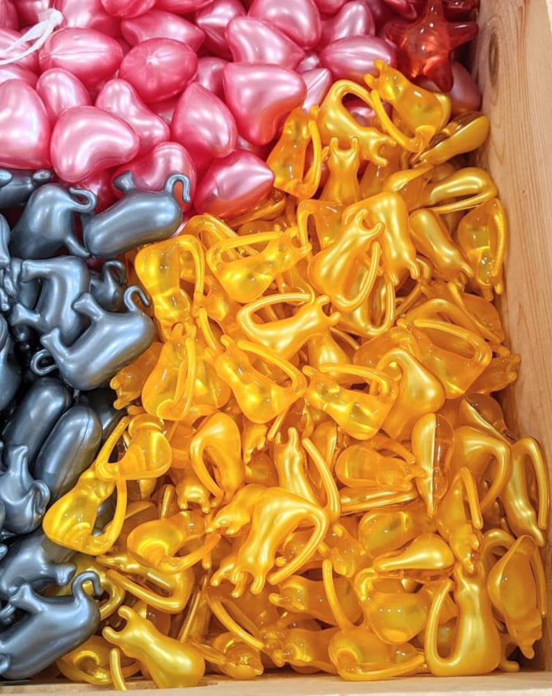 K&ouml;nnte beinhalten: Nahaufnahme eines Stapels kleiner, goldener, herzf&ouml;rmiger Kapseln. Die Kapseln sind in einem zuf&auml;lligen Muster angeordnet und alle gleich gro&szlig; und gleich geformt. Die Kapseln bestehen aus einem klaren, gl&auml;nzenden Material und haben einen leichten Schimmer.