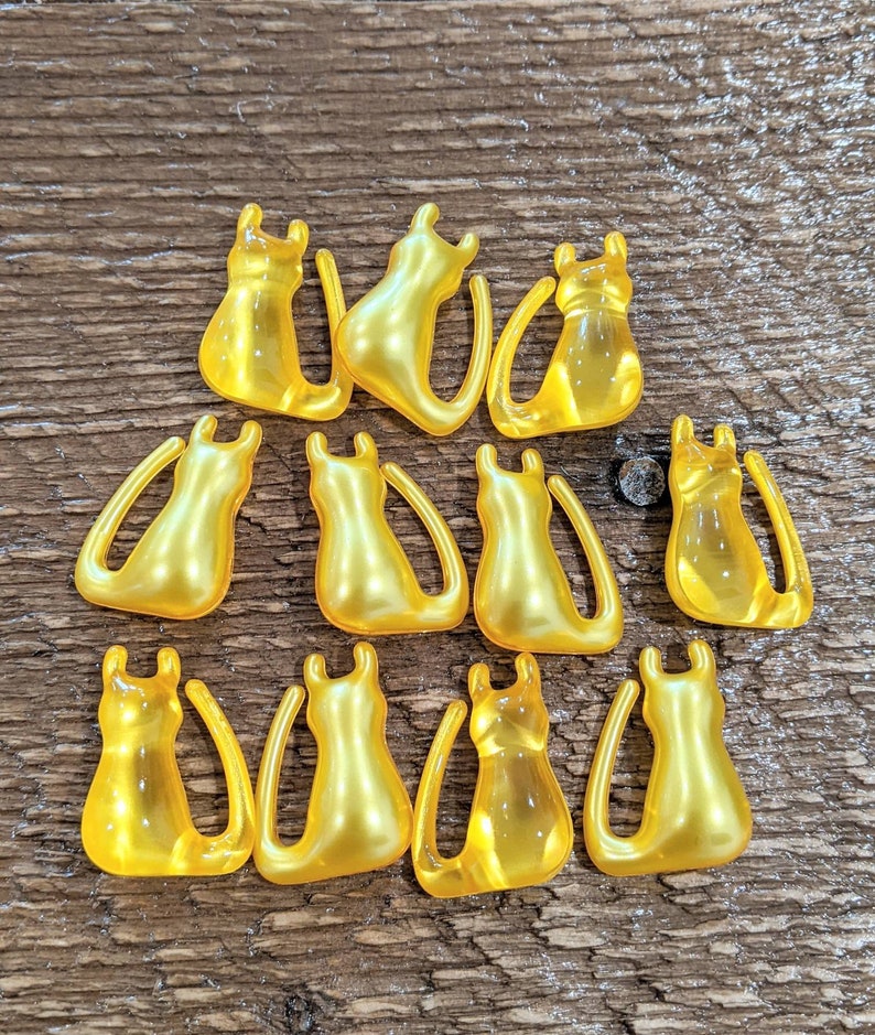 K&ouml;nnte beinhalten: Eine Sammlung von 12 gelben Katzenfiguren aus Kunststoff. Die Katzen sind alle in die gleiche Richtung ausgerichtet und haben eine gl&auml;nzende Oberfl&auml;che.