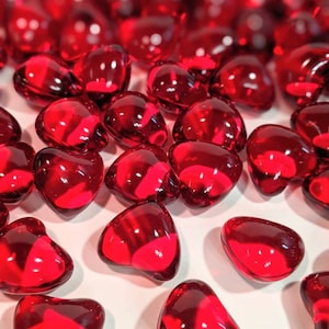 May include: A scattering of small, red, heart-shaped glass beads. The beads are translucent and have a glossy finish.