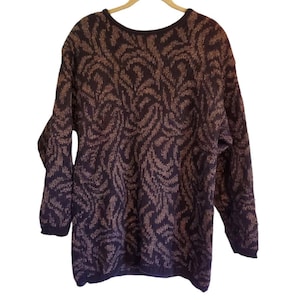 May include: A dark purple sweater with a brown and tan pattern. The sweater has long sleeves and a crew neck. The pattern is a repeating design of curved lines. The sweater is hanging on a wooden hanger.