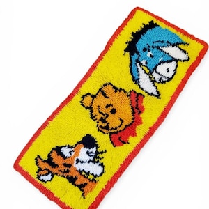 May include: A rectangular, yellow rug featuring three cartoon characters: a blue donkey, an orange bear, and an orange and black tiger. The rug has a red border.