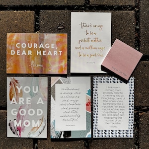 May include: A set of six inspirational cards with quotes about motherhood. The cards feature different backgrounds and designs, including feathers, abstract patterns, and a pink sticky note with the text "You've Got This!" The quotes include: "Courage, Dear Heart", "You Are A Good Mom", "Motherhood is messy. And challenging. And crazy. And sleepless. And giving. And still unbelievably beautiful", "There's no way to be a perfect mother and a million ways to be a good one", and "I think every working mum probably feels the same thing: You go through big chunks of time where you're just thinking, 'This is impossible - oh, this is impossible.' And then you just keep going and keep going and keep going, and you sort of do the impossible."