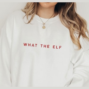 May include: White sweatshirt with the text "WHAT THE ELF" printed in red.