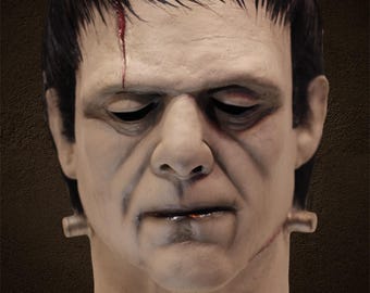 Può includere: Maschera dettagliata del mostro di Frankenstein, con incarnato pallido, capelli scuri e cicatrici cucite. La maschera ha una fronte prominente, occhi infossati e bulloni sul collo, catturando l'aspetto iconico del personaggio. Un costume o un accessorio di Halloween.