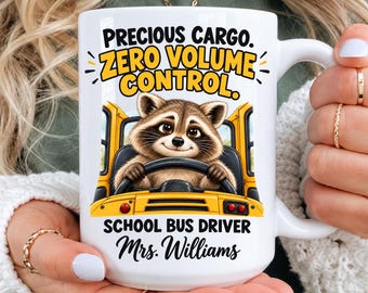 May include: A white ceramic mug featuring a graphic of a raccoon driving a yellow school bus. The text reads: PRECIOUS CARGO. ZERO VOLUME CONTROL. SCHOOL BUS DRIVER Mrs. Williams. The design includes black and yellow lettering.