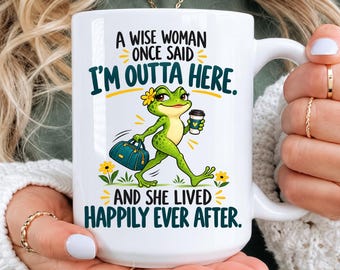 May include: A white ceramic mug featuring a green frog illustration, a teal travel bag, and yellow flowers. The text reads: A WISE WOMAN ONCE SAID I'M OUTTA HERE. AND SHE LIVED HAPPILY EVER AFTER. The frog holds a coffee cup with a blue heart.