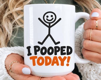 May include: A white ceramic mug featuring a black stick figure illustration with arms and legs raised. Below the figure, the text reads I POOPED in black letters and TODAY! in orange letters. The mug has a standard handle and a smooth finish.