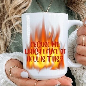 Puede incluir: Taza de cerámica blanca con un diseño de llamas rojas y naranjas y el texto "Disculpe, ¿en qué nivel del infierno estamos?"