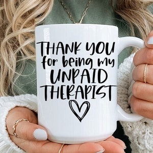May include: White ceramic mug with black text that reads "Thank you for being my unpaid therapist" with a small heart symbol.