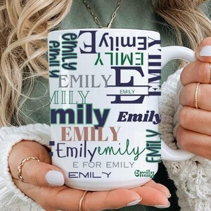 May include: White ceramic mug with the name "Emily" repeated in various fonts and colours, including green, purple, and brown. The mug has a black handle.