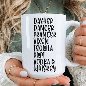Könnte beinhalten: Eine weiße Keramiktasse mit schwarzem Text, der "Dasher Dancer Prancer Vixen Tequila Rum Vodka & Whiskey" lautet.