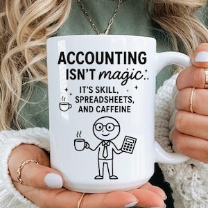 May include: White ceramic mug with the text "ACCOUNTING ISN'T magic" and the words "IT'S SKILL, SPREADSHEETS, AND CAFFEINE". The mug features a stick figure holding a coffee cup and calculator. The mug is held by a person.