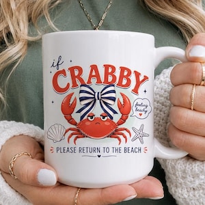 May include: White ceramic mug with the text "if CRABBY PLEASE RETURN TO THE BEACH". The mug features a red crab with a blue bow, a seashell, and a starfish design. The mug has a large handle.