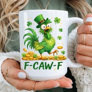 May include: White ceramic mug featuring a green rooster wearing a leprechaun hat, surrounded by shamrocks and gold coins. The mug has the text "F-CAW-F" in green. A fun and festive St. Patrick's Day themed mug.