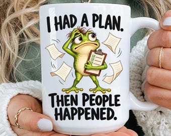 May include: A white ceramic mug featuring a cartoon frog holding a clipboard with scattered papers. The text above the frog reads I HAD A PLAN. and the text below reads THEN PEOPLE HAPPENED. The mug has a large handle and a smooth, glossy finish.