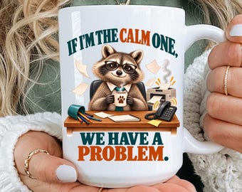 May include: A white ceramic mug featuring a graphic of a raccoon wearing glasses at a desk with a computer and phone. The text reads, IF I'M THE CALM ONE, WE HAVE A PROBLEM. The mug has a handle on the right side and a smooth, glossy finish.
