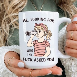 May include: White ceramic mug with a humorous illustration of a girl looking through a telescope. The mug features the text "ME, LOOKING FOR WHO THE FUCK ASKED YOU" in black lettering. The girl is wearing a pink bow and a pink and white striped shirt.