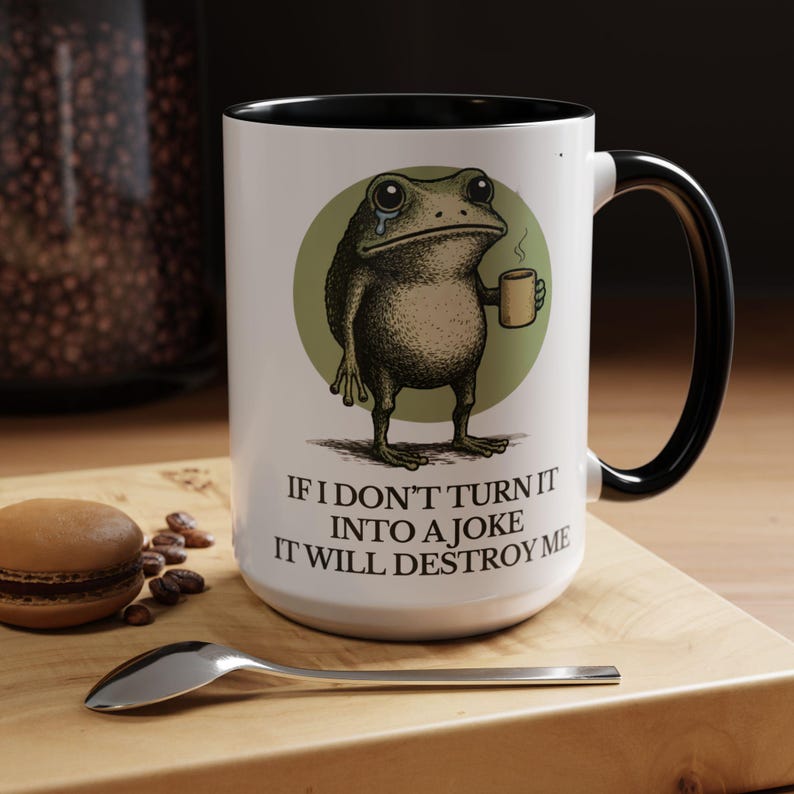 Puede incluir: Taza de cer&aacute;mica blanca con asa e interior negros. La taza presenta una ilustraci&oacute;n desgastada de una rana llorando sosteniendo una taza de caf&eacute;, sobre un c&iacute;rculo verde. El texto dice: "SI NO LO CONVIERTO EN UNA BROMA, ME DESTRUIR&Aacute;".